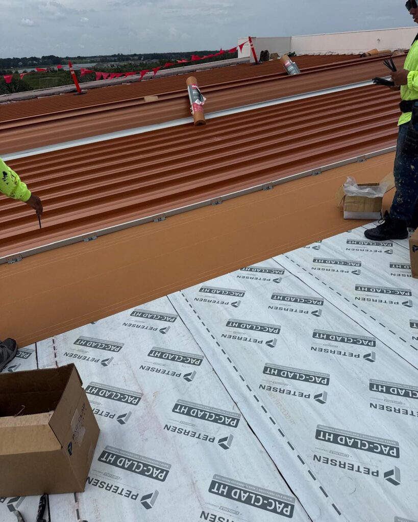 Copper-colored metal roof panels being fastened by the JHI Roofing team